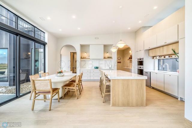 kitchen with light wood-type flooring, backsplash, light countertops, arched walkways, and a center island