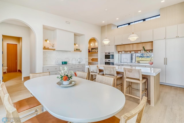 dining area featuring arched walkways, light wood-style floors, and recessed lighting