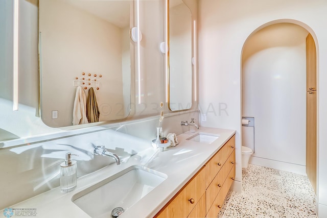 full bath featuring a sink, double vanity, toilet, and speckled floor