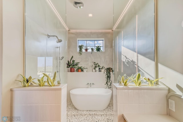 bathroom featuring speckled floor, tile walls, walk in shower, and a freestanding tub