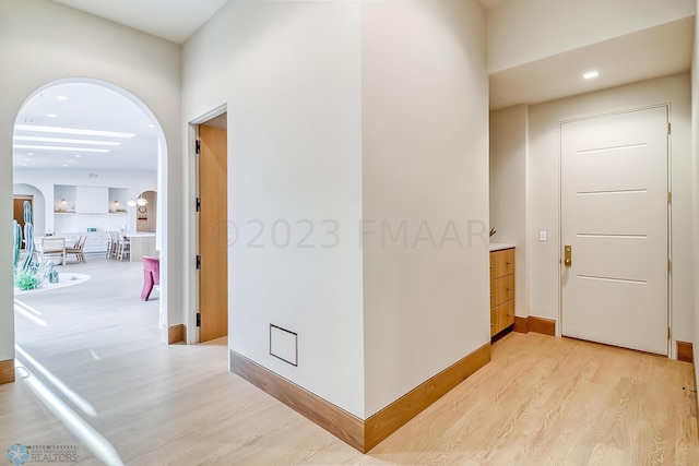 hall featuring light wood-style floors, baseboards, and arched walkways