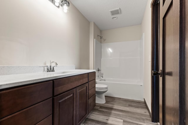 full bathroom featuring hardwood / wood-style floors, vanity,  shower combination, toilet, and a textured ceiling