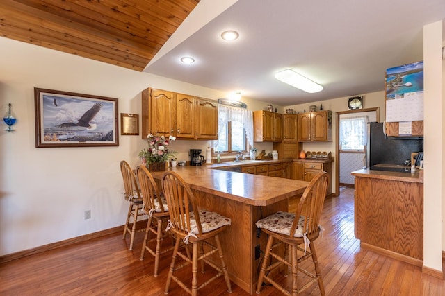 kitchen featuring sink, stainless steel refrigerator, wood-type flooring, a kitchen bar, and kitchen peninsula