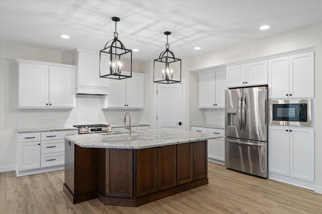 kitchen with sink, a kitchen island with sink, stainless steel refrigerator with ice dispenser, white cabinets, and built in microwave