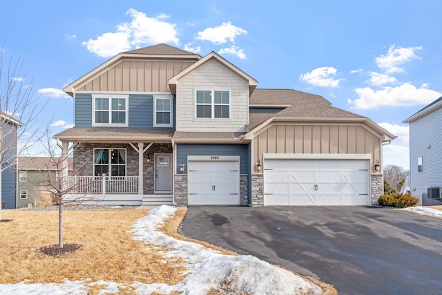 craftsman-style home with board and batten siding, covered porch, driveway, and stone siding