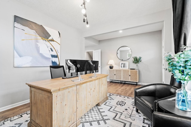 office with light wood-style floors, track lighting, baseboards, and a textured ceiling