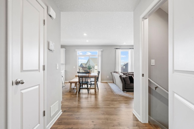 hallway featuring visible vents, baseboards, wood finished floors, a textured ceiling, and recessed lighting