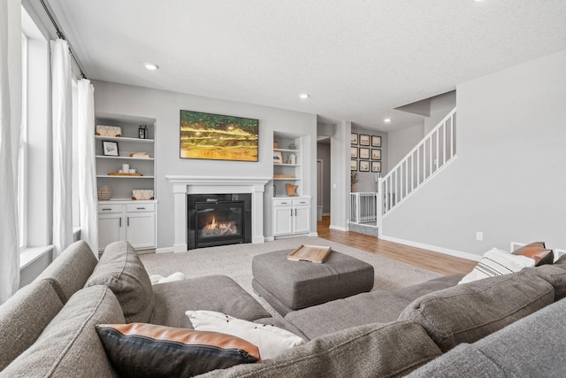 living area with built in features, a glass covered fireplace, a textured ceiling, baseboards, and stairs