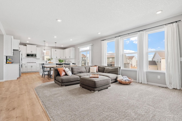 living room featuring light wood-type flooring, a textured ceiling, baseboards, and recessed lighting