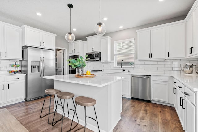 kitchen with stainless steel appliances, dark wood-type flooring, white cabinets, a sink, and a kitchen bar