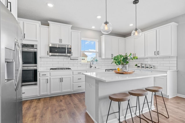 kitchen with stainless steel appliances, white cabinetry, a sink, and wood finished floors