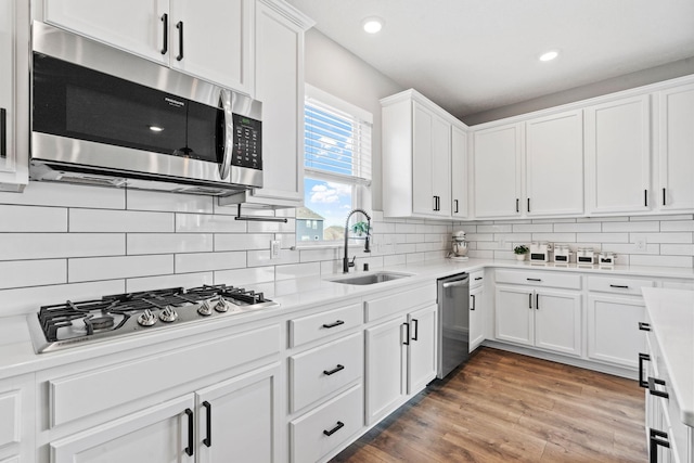 kitchen with light countertops, light wood-style flooring, appliances with stainless steel finishes, white cabinetry, and a sink