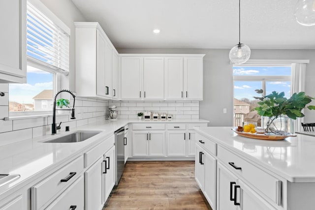 kitchen featuring a sink, light countertops, light wood-type flooring, white cabinetry, and stainless steel dishwasher