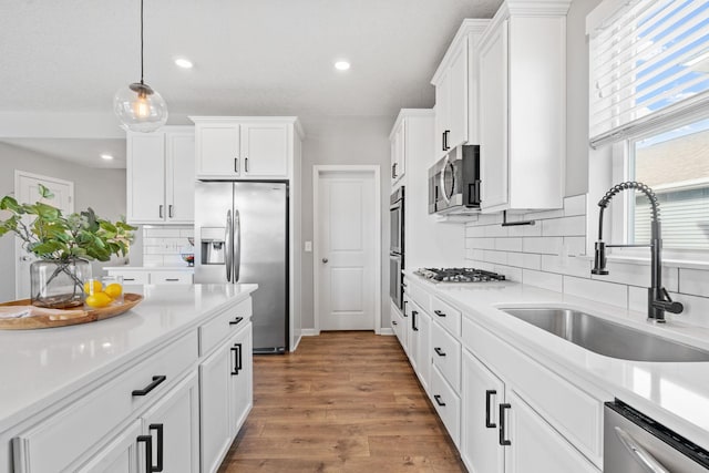 kitchen with wood finished floors, a sink, white cabinetry, light countertops, and appliances with stainless steel finishes