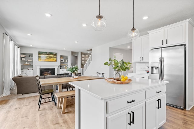 kitchen featuring light wood finished floors, stainless steel fridge, a glass covered fireplace, open floor plan, and light countertops