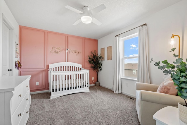 bedroom with a crib, light carpet, visible vents, a ceiling fan, and a textured ceiling