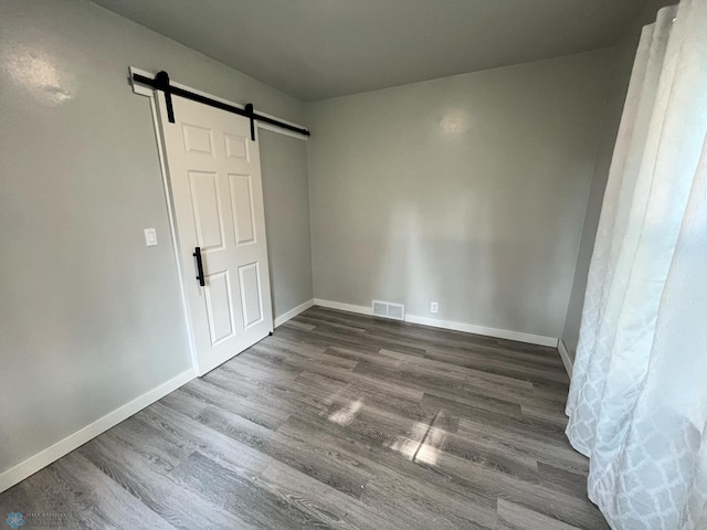 unfurnished bedroom with a barn door and dark wood-type flooring