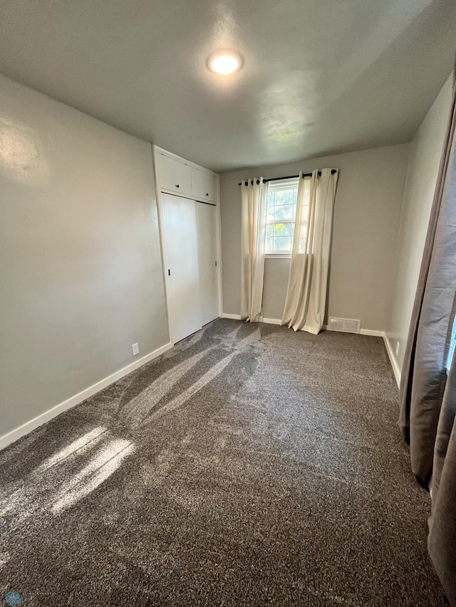 unfurnished bedroom with dark carpet and a closet