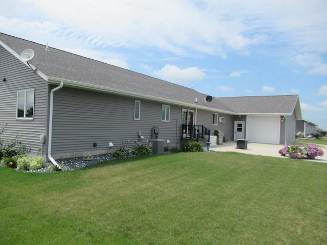 rear view of property with central air condition unit, roof with shingles, a garage, and a lawn