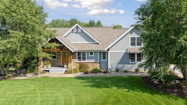 craftsman-style home with stone siding, covered porch, roof with shingles, and a front yard