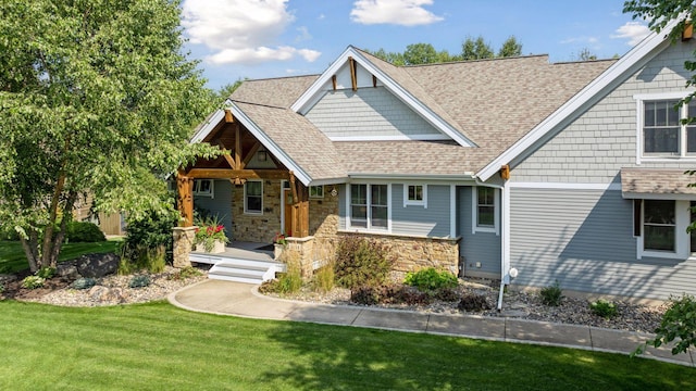 craftsman inspired home featuring stone siding, covered porch, a shingled roof, and a front yard