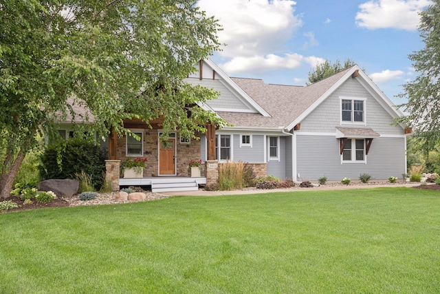 view of front of home with a front lawn, covered porch, stone siding, and roof with shingles