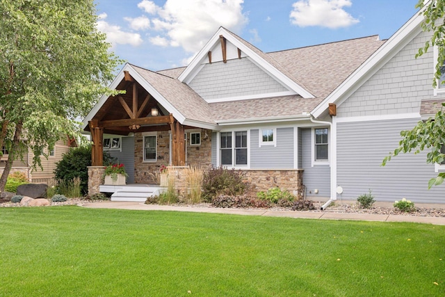 craftsman-style home with stone siding, roof with shingles, covered porch, and a front yard