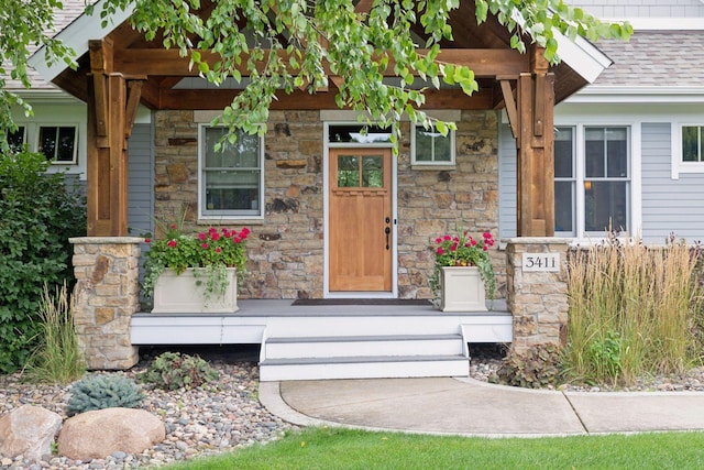 view of exterior entry with stone siding and a shingled roof