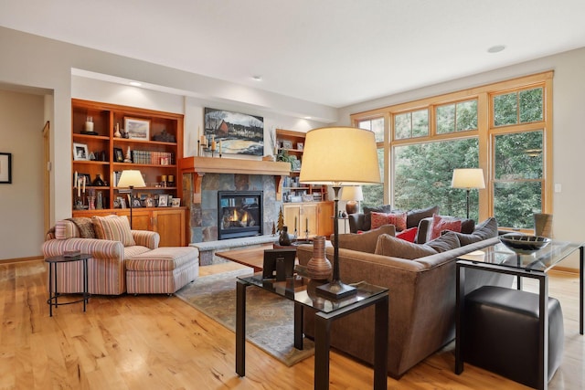 living room with a tiled fireplace, built in features, baseboards, and light wood-type flooring