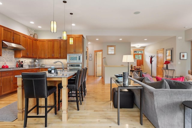 kitchen with tasteful backsplash, under cabinet range hood, open floor plan, appliances with stainless steel finishes, and a kitchen breakfast bar