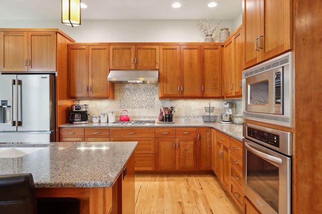 kitchen featuring light stone counters, tasteful backsplash, under cabinet range hood, and stainless steel appliances