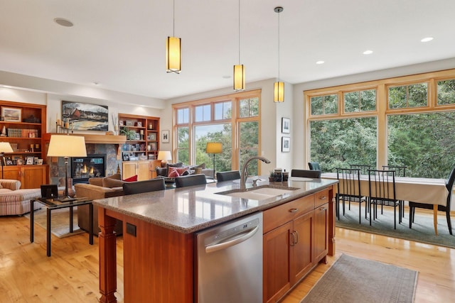 kitchen featuring stainless steel dishwasher, a tiled fireplace, light wood-style floors, and a sink