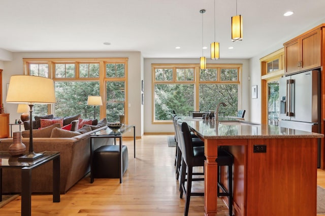 kitchen with a center island with sink, dark stone counters, a sink, light wood-style floors, and decorative light fixtures