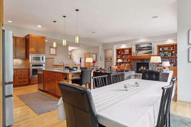 dining space featuring recessed lighting, a warm lit fireplace, light wood-style floors, and built in shelves