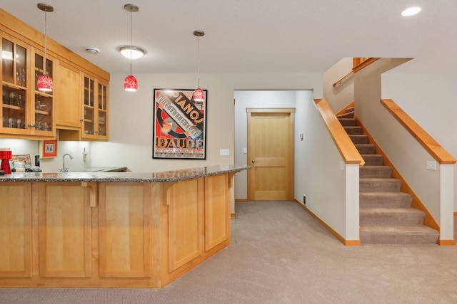 kitchen with a kitchen bar, dark stone counters, glass insert cabinets, baseboards, and light colored carpet