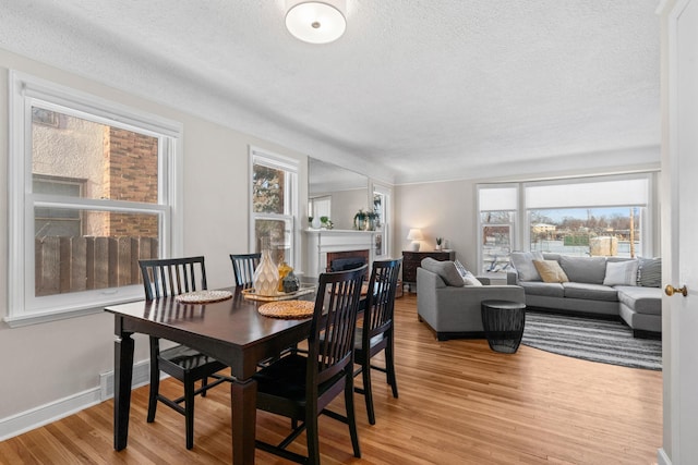 dining room with a textured ceiling, a brick fireplace, and light hardwood / wood-style flooring