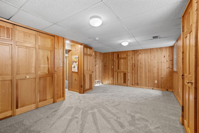 basement with light carpet, a drop ceiling, and wooden walls