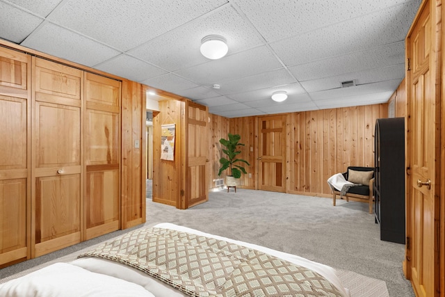 bedroom featuring light carpet, a closet, a paneled ceiling, and wooden walls