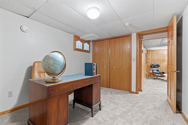 carpeted home office featuring a paneled ceiling and wood walls