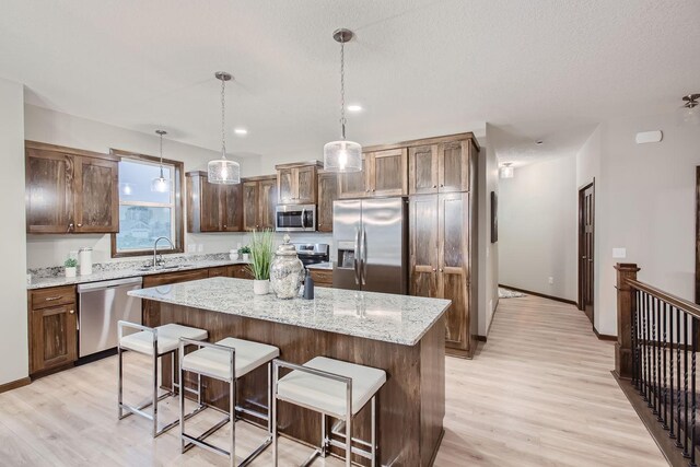 kitchen with appliances with stainless steel finishes, decorative light fixtures, light wood-type flooring, a breakfast bar area, and a center island