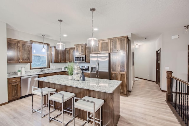 kitchen featuring stainless steel appliances, a center island, light wood-style flooring, and a kitchen bar