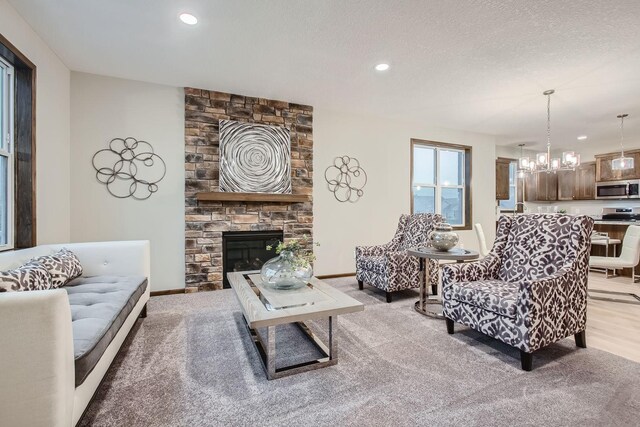 living room featuring a fireplace, light hardwood / wood-style floors, a textured ceiling, and an inviting chandelier