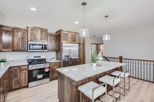 kitchen with appliances with stainless steel finishes, decorative light fixtures, light hardwood / wood-style floors, a center island, and a breakfast bar