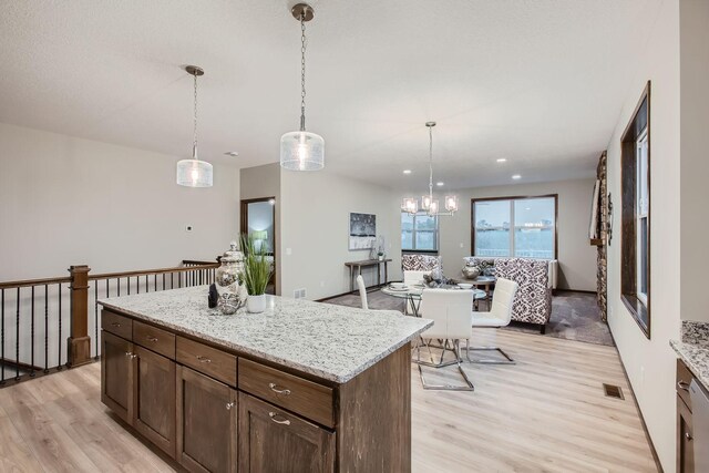 kitchen featuring a kitchen island, light hardwood / wood-style floors, light stone countertops, and hanging light fixtures