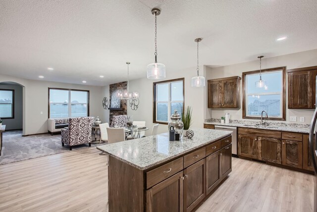 kitchen featuring sink, decorative light fixtures, light wood-type flooring, light stone countertops, and stainless steel dishwasher