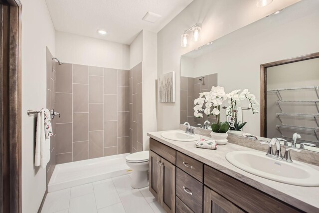 bathroom featuring double sink vanity, tiled shower, tile patterned floors, a textured ceiling, and toilet