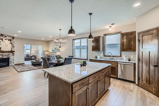 kitchen featuring light wood-type flooring, a sink, stainless steel dishwasher, open floor plan, and a fireplace