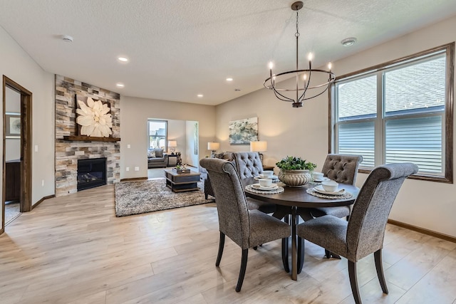 dining area with a textured ceiling, a stone fireplace, and light wood finished floors