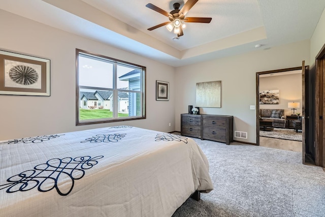 carpeted bedroom with visible vents, baseboards, a tray ceiling, and a ceiling fan