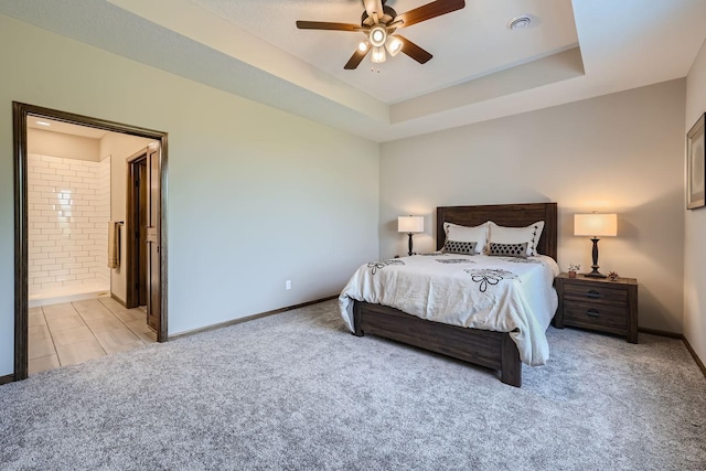 bedroom featuring light carpet, ensuite bathroom, a raised ceiling, and baseboards